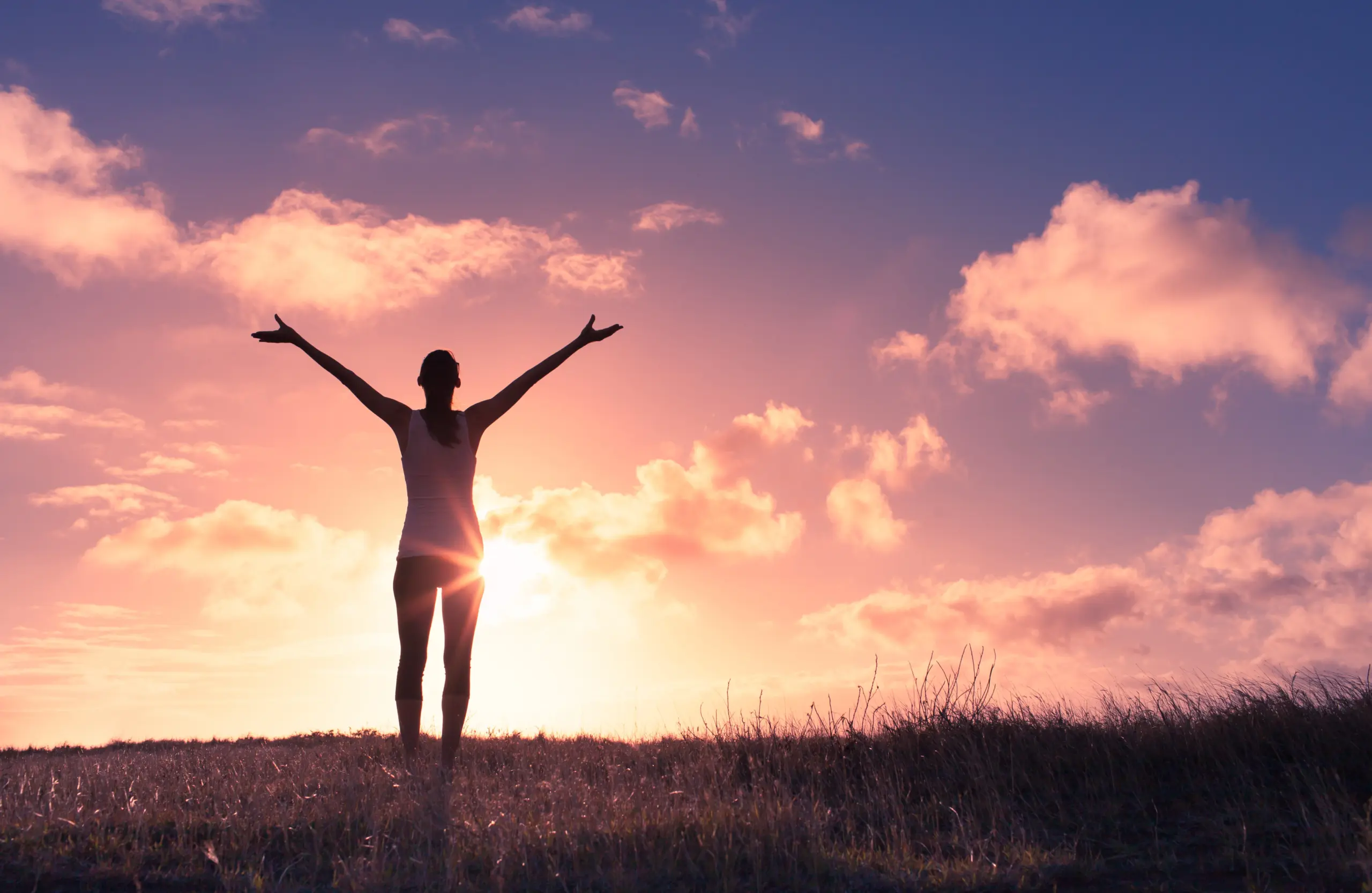 Happy woman with arms up in the sunset