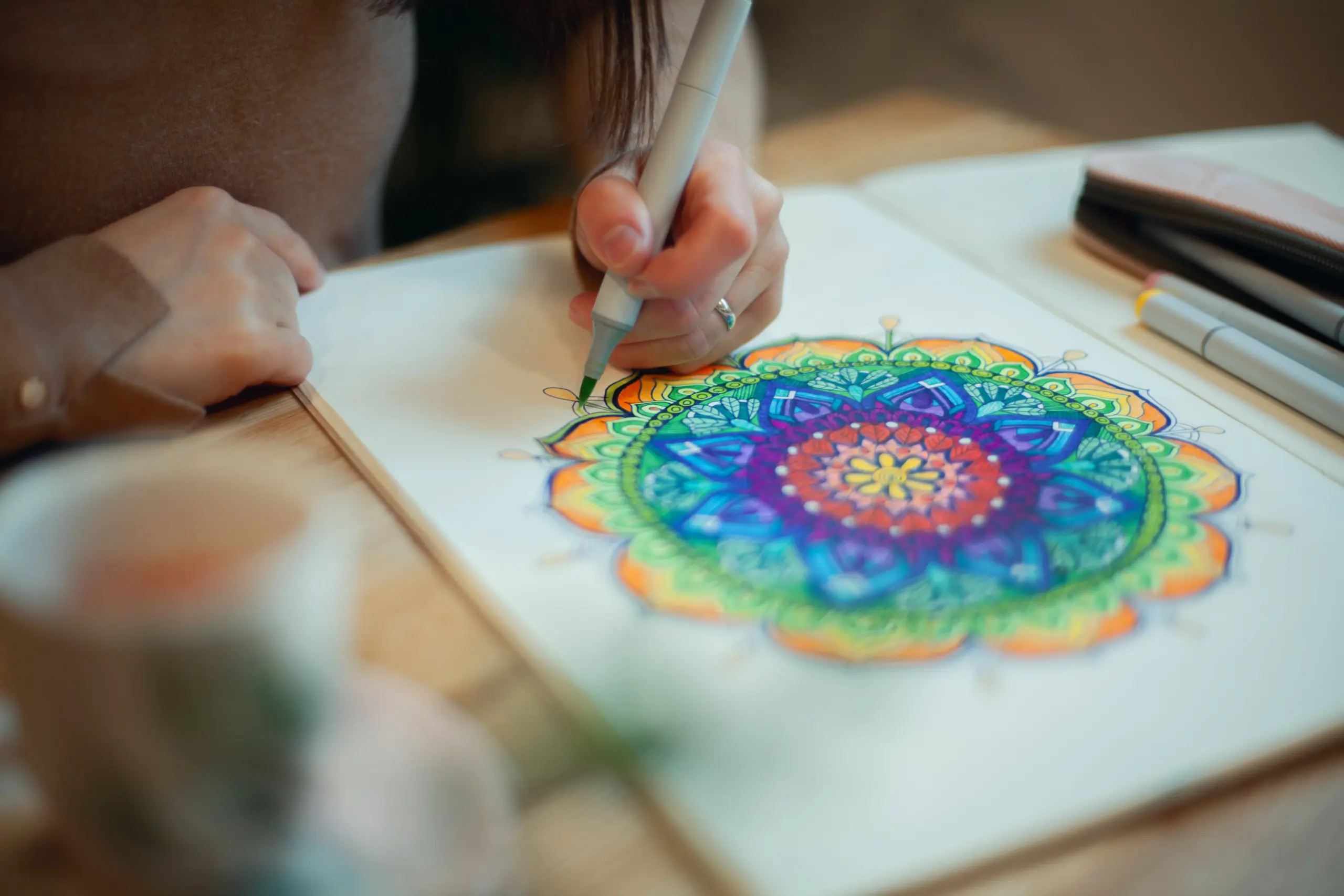 Young woman colouring mandala with markers and white rosary on table